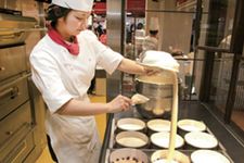 Proses pembuatan cheesecake di Osaka, Jepang. Setelah selesai diaduk, adonan dimasukkan ke dalam masing-masing loyang kertas dari jarak yang cukup tinggi.