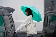 Ilustrasi perempuan memakai payung dan jaket sedang membuka mobil.