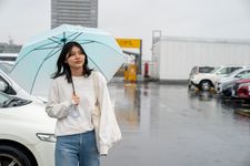 Wanita mengenakan outfit blus panjang sedang memakai payung.
