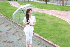 Wanita mengenakan outfit blus sedang memakai payung.