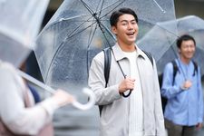 Seorang pria mengenakan outfit kemeja dan jaket sedang memakai payung.