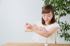 Seorang wanita mengenakan outfit blus tipis sedang mengaplikasikan krim UV.