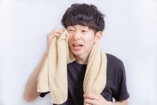 Seorang pria mengenakan outfit kaos sedang menyeka keringat dengan handuk.