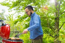 Seorang pria mengenakan outfit kemeja jeans sedang barbeque.