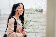 Seorang wanita mengenakan outfit blouse dan payung di kala hujan turun.