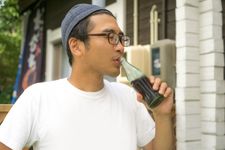 Seorang pria dengan outfit memakai kaos dan topi sedang minum soda.