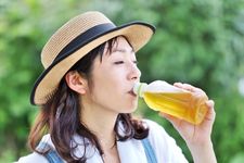 Seorang wanita memakai outfit wearpack dan topi sedang minum.