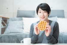 Seorang wanita memakai outfit kaos santai sedang menikmati snack.