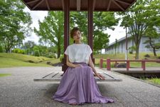 Seorang wanita memakai outfit blus dan rok panjang sedang bersantai.
