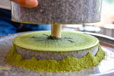 Pemandangan dekat dari sebuah penggilingan batu granit tradisional yang menggiling daun tencha menjadi bubuk matcha halus. Foto ini diambil di Uji, Prefektur Kyoto, Jepang.