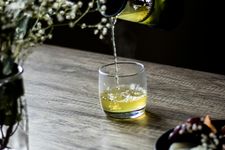 Foto seseorang menuangkan teh hijau ke dalam gelas minum.