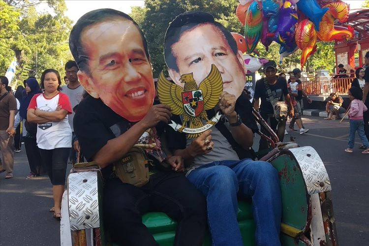 Warga memakai topeng Jokowi dan Prabowo naik becak di car free day (CFD) Jalan Slamet Riyadi Solo, Jawa Tengah, Minggu (14/7/2019).