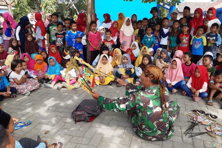 Serma Paijan Babinsa Kalikondang, Kabupaten Demak , Jateng,  memperlihatkan kemampuannya mendalang di depan anak - anak, di sela - sela kegiatan TMMD, Jumat (19/7/2019) siang.