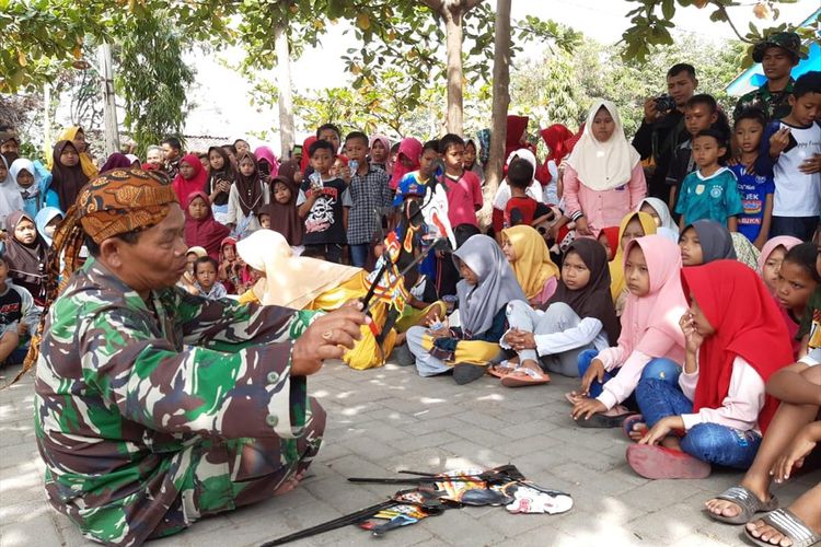 Serma Paijan Babinsa Kalikondang, Kabupaten Demak , Jateng,  memperlihatkan kemampuannya mendalang di depan anak - anak, di sela - sela kegiatan TMMD, Jumat (19/7/2019) siang.