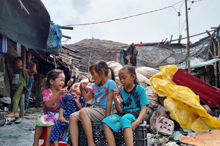 Sejumlah anak-anak tengah asyik bermain, dan makan camilan di dekat gundukan sampah di landfill TPST Bantargebang, Bekasi Minggu (11/12/2023). Tidak terlihat sedikit pun mereka terganggu dengan polusi udara berupa debu dan aroma tak sedap yang keluar tumpukan sampah tersebut.