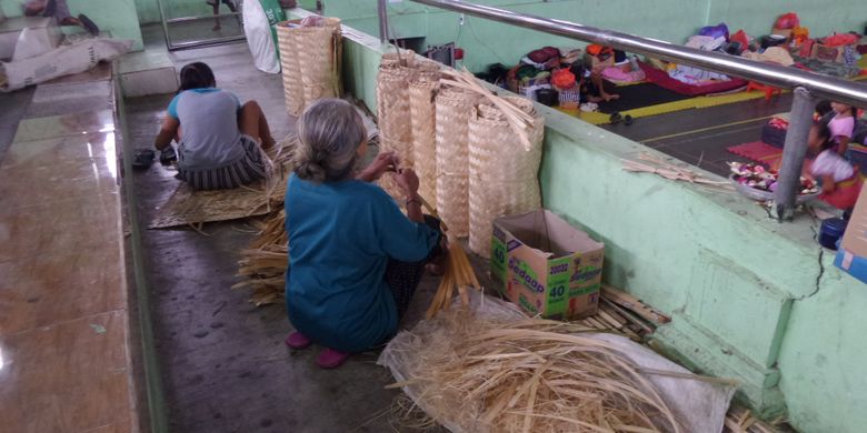 Seorang nenek dan cucunya yang mengungsi di GOR Swecapura, Klungkung, tetap bekerja membuat anyaman bide agar tetap menghasilkan uang sekaligus menghilangkan jenuh.