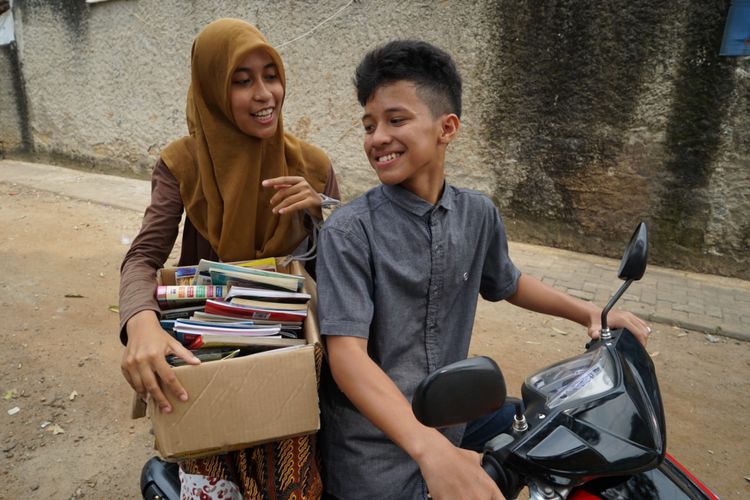 Dua orang relawan dari komunitas Warung Baca Mata Air membawa kardus berisi buku untuk dipinjamkan secara gratis ke anak-anak Kampung Serut. Mereka menamakan kegiatan itu Modus atau Motor Kardus.