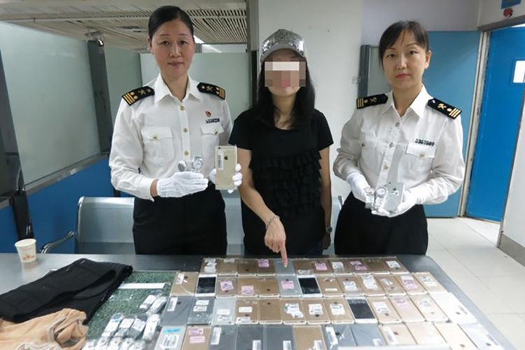 Wanita penyelundup asal China (tengah) diapit petugas bea cukai Shenzen dengan barang bukti berupa 102 unit iPhone dan 15 jam tangan mewah yang coba diselundupkannya ke China dari Hong Kong.
