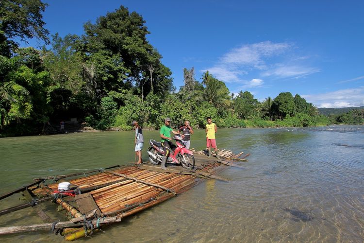 Sebuah rakit mengangkut motor dan warga menyeberangi sungai di Bulango Ulu, Kabupaten Bone Bolango, Gorontalo, Selasa (5/9/2017). Jasa rakit penyeberangan di desa pelosok tersebut memiliki tarif Rp1.000 per orang atau motor karena belum adanya jembatan penyeberangan. 