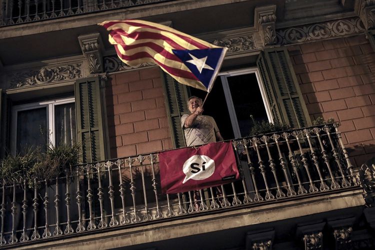 Seorang pria melambaikan bendera Estelada (bendera Catalan pro-kemerdekaan) dari sebuah balkon setelah penutupan tempat pemungutan suara Espai Jove La Fontana, Barcelona, Spanyol, Minggu (1/10/2017), pada hari referendum kemerdekaan Catalonia. Pemerintah Spanyol menentang referendum Catalonia dan melarang pelaksanaan pemungutan suara yang berakhir kericuhan antara otoritas keamanan dan warga.