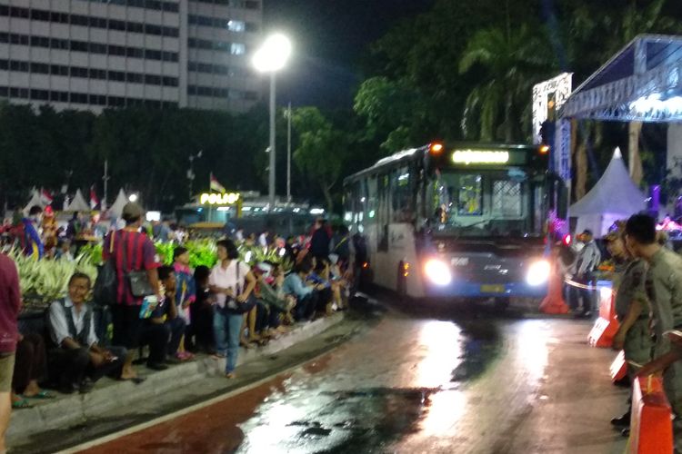 Bus Transjakarta melewati pengunjung car free night yang tengah menikmati panggung hiburan, Minggu (31/12/2017)