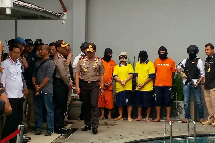 Para tersangka mengenakan baju tahanan dikawal oleh petugas kepolisian di tempat produksi miras oplosan jenis gingseng di Jalan By Pass RT03/08 Cicalengka Wetan, Kabupaten Bandung, Kamis (19/4/2018). 