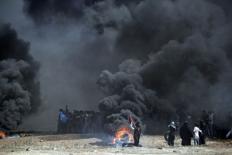 Warga Palestina membakar ban saat terjadi bentrokan dengan pasukan Israel di dekat perbatasan antara jalur Gaza dan Israel, di sebelah timur Kota Gaza, Senin (14/5/2018). Otoritas Palestina menyebut pasukan Israel telah menewaskan 55 orang dan melukai 2.700 orang dalam aksi protes dan bentrokan menentang pembukaan Kedutaan Besar Amerika Serikat di Yerusalem.