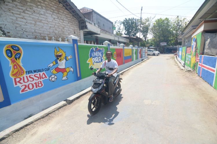 Jalan akses desa di Desa Tentenan Timur pagar rumah warga di kanan-kiri dicat dengan bendera dan gambar maskot serta pemain negara kontestan piala dunia.