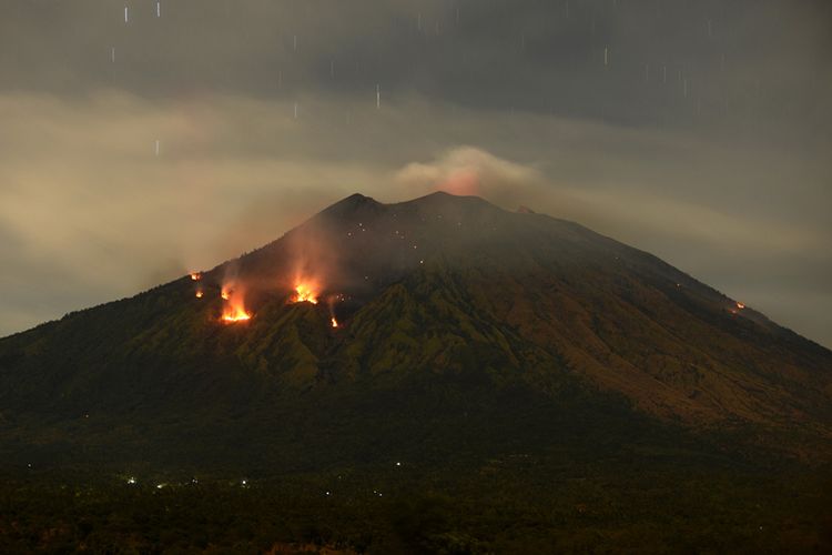 Api membakar hutan lereng Gunung Agung setelah terjadinya lontaran batu pijar dari kawah, terlihat dari Desa Tulamben, Karangasem, Bali, Selasa (3/7/2018). Pusat Vulkanologi dan Mitigasi Bencana Geologi mencatat terjadinya erupsi Gunung Agung dengan tinggi kolom abu mencapai 2.000 meter yang disertai lontaran batu pijar sejauh dua kilometer.