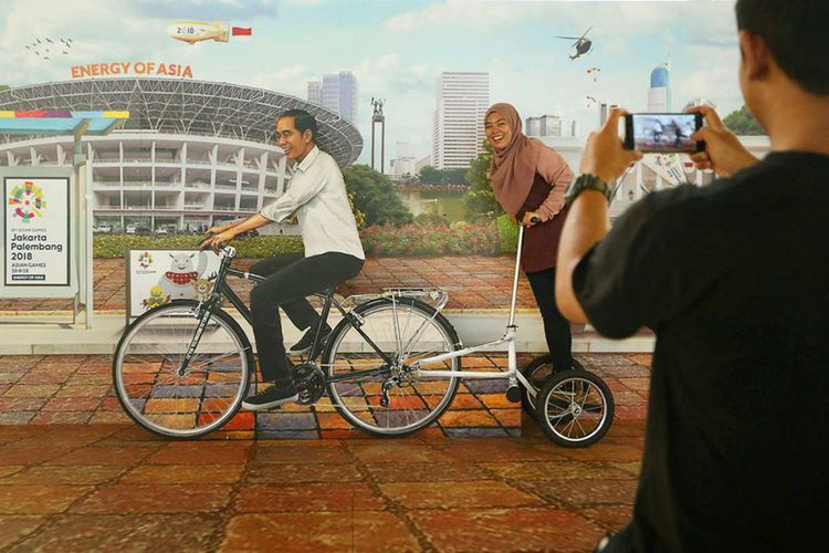 Seorang penumpang tengah berpose dengan foto Jokowi dan hiasan bertuliskan Asian Games 2018 di Terminal 3 Keberangkatan Bandara SOekarno-Hatta, Tangerang, Banten, Kamis (5/07/2018). PT Angkasa Pura AP (II) selaku pengelola bandara menyatakan siap memfasilitasi kedatangan dan kepulangan peserta Asian Games 2018 dengan menyiapkan sarana dan prasarana di tiga bandara yakni Bandara Soekarno Hatta, Bandara Sultan Mahmud Badaruddin II Palembang dan Husein Sastranegara Bandung.