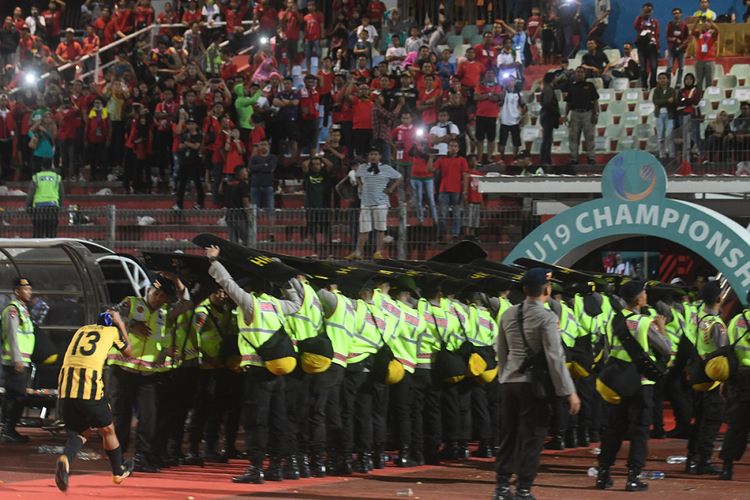 Petugas keamanan berusaha melindungi pesepak bola  Malaysia U-19 Mohamad Izzuddin (kiri) dari lemparan suporter Indonesia usai laga semifinal Piala AFF U-19 di Gelora Delta Sidoarjo, Sidoarjo, Jawa Timur, Kamis (12/7/2018). Indonesia kalah adu penalti dari Malaysia dengan skor 3-4.