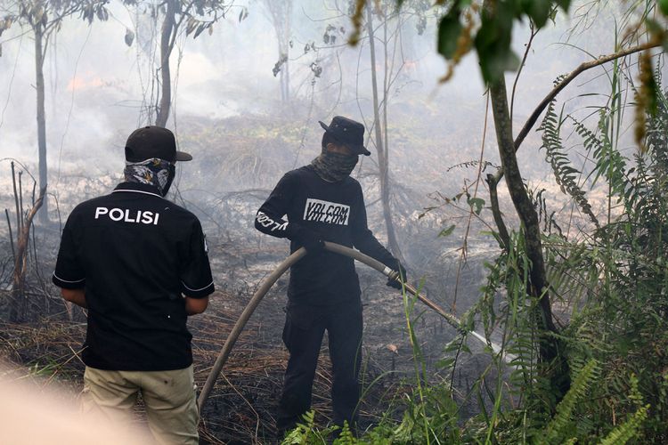 Petugas kepolisian dari Polresta Pontianak bersama pemadam kebakaran swasta saat berupaya memadamkan api di lahan gambut yang mendekati permukiman warga di Jalan Purnama II, Pontianak (20/8/2018).