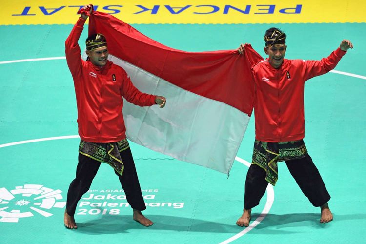 Pasangan pesilat Indonesia Yola Primadona Jampil (kiri) dan Hendy (kiri) membentangkan bendera merah putih saat merayakan kemenangan usai meraih medali emas nomor ganda putra pencak silat seni Asian Games 2018 di Padepokan Pencak Silat Taman Mini Indonesia Indah (TMII), Jakarta, Senin (27/8/2018).