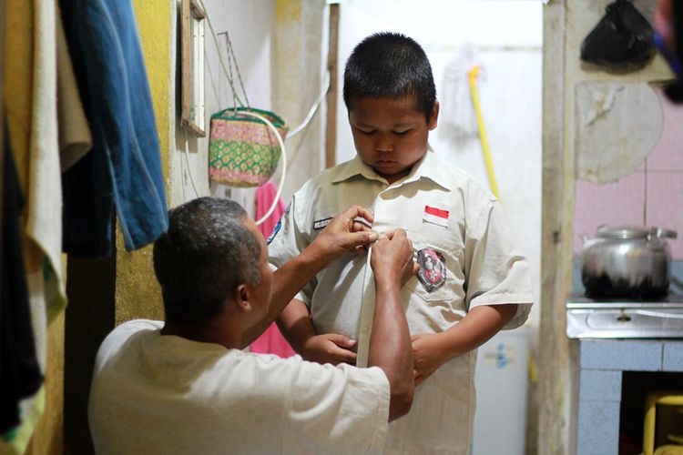 Darsono (53) ayah Nursaka membantu memakaikan pakaian seragam sekolah, Kamis (13/9/2018).