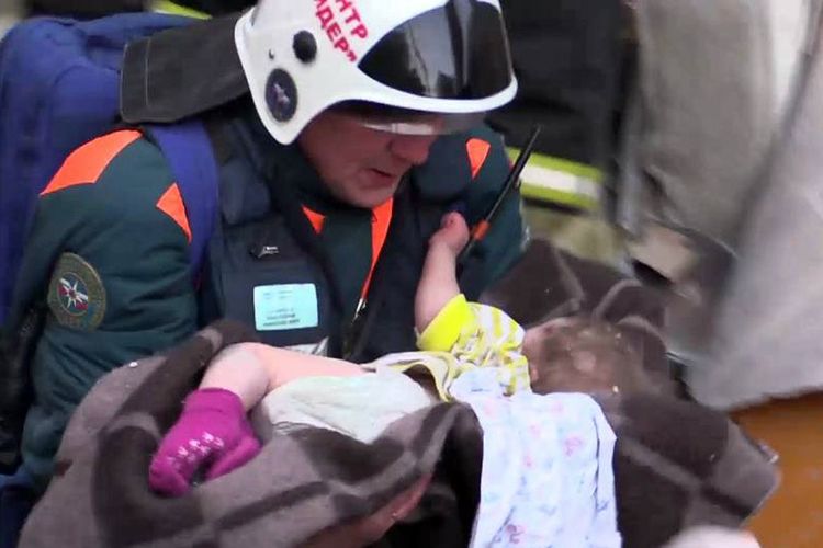 Foto yang dirilis Kementerian Darurat Rusia pada 1 Januari 2018 menunjukkan tim penyelamat menggendong seorang bayi berusia 10 bulan yang ditemukan masih hidup di reruntuhan apartemen yang hancur akibat ledakan di Magnitogorsk, kawasan Ural, pada Senin (31/12/2018).