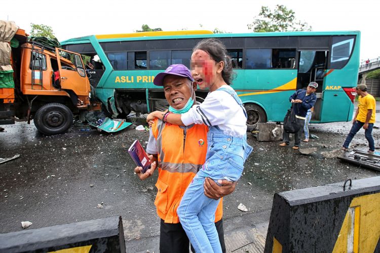 Petugas mengevakuasi seorang bocah saat terjadi kecelakaan bus Asli Prima di Gerbang Tol Cikupa, Tangerang, Banten, Minggu (13/01/2019). Bus Asli Prima yang melaju dari arah Jakarta keluar jalur menabrak truk yang melaju menuju Jakarta. Akibat kecelakaan ini dua orang luka berat dan belasan lainnya luka ringan.