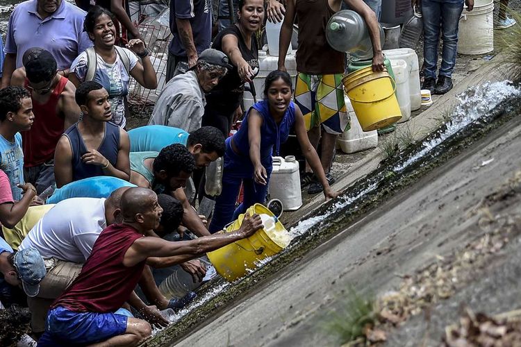 Orang-orang mengumpulkan air dari pipa rusak yang mengalir ke saluran pembuangan limbah di Sungai Guaire, Caracas, Venezuela, Senin (11/3/2019), dampak pemadaman listrik masif di negara itu. Di tengah krisis yang melanda Venezuela, pemadaman listrik massal yang terjadi berhari-hari di sejumlah kawasan negara itu menimbulkan banyak kekacauan seperti penjarahan hingga kesulitan air.