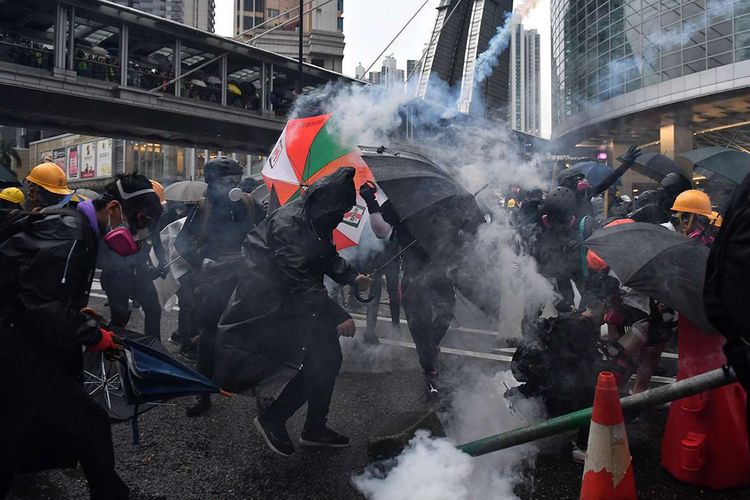Pengunjuk rasa pro-demokrasi berusaha melindungi diri mereka dari lemparan gas air mata yang ditembakkan polisi, saat terjadi bentrokan di Tseun Wan, Hong Kong, Minggu (25/8/2019). Aksi protes telah bergulir selama 3 bulan terakhir di Hong Kong, dimulai ketika Kepala Eksekutif Hong Kong Carrie Lam memperkenalkan undang-undang yang bisa mengekstradisi kriminal ke China daratan.