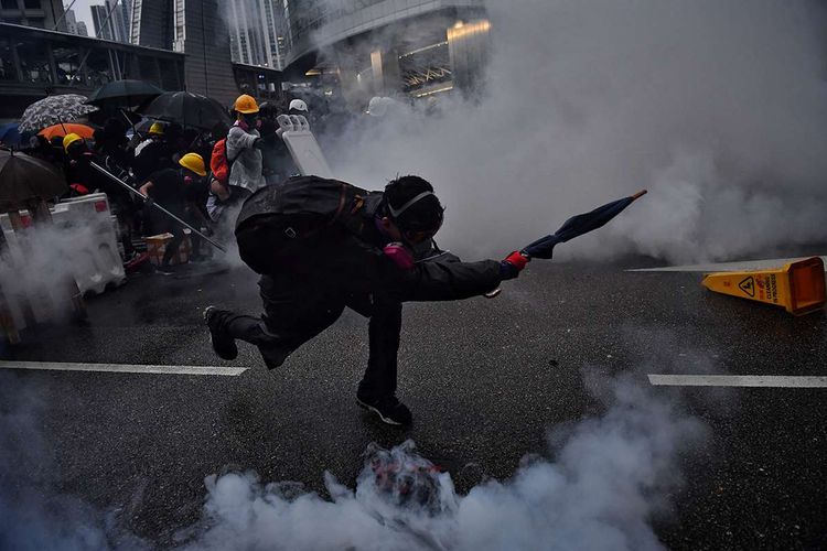 Pengunjuk rasa pro-demokrasi berusaha mengembalikan gas air mata ke arah polisi, saat terjadi bentrokan di Tseun Wan, Hong Kong, Minggu (25/8/2019). Aksi protes telah bergulir selama 3 bulan terakhir di Hong Kong, dimulai ketika Kepala Eksekutif Hong Kong Carrie Lam memperkenalkan undang-undang yang bisa mengekstradisi kriminal ke China daratan.