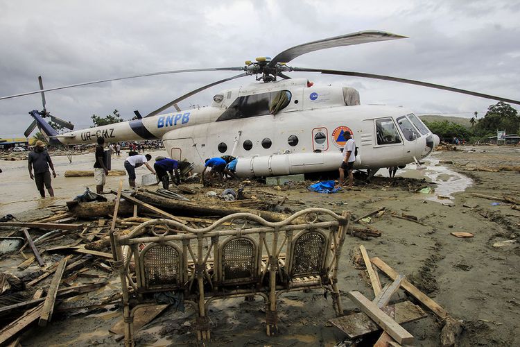 Sejumlah warga berada di dekat helikopter yang bergeser dari tempatnya akibat banjir bandang di Sentani, Kabupaten Jayapura, Papua, Minggu (17/3/2019). Jumlah korban bencana banjir bandang yang terjadi pada Sabtu (16/3/2019) malam kemarin, hingga data yang masuk pada Minggu sore, terus bertambah menjadi 63 orang.
