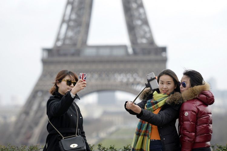 Tiga turis China tengah melakukan selfie dengan latar belakang Menara Eiffel di Paris, Perancis.