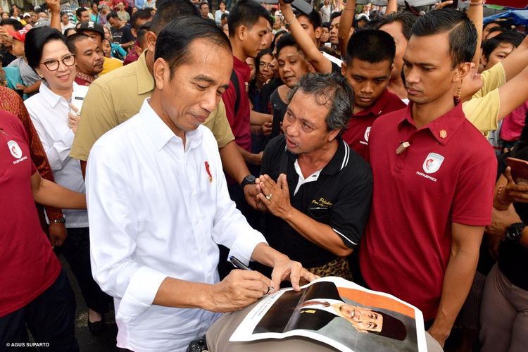 Presiden Joko Widodo membubuhkan tanda tangan di atas selembar foto yang diberikan warga Bali, Jumat (14/6/2019). Uniknya, alas foto itu adalah punggung asisten ajudan AKP Syarif Muhanmad Fitriansyah. 