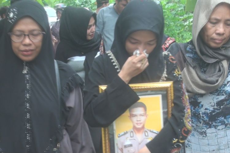 Mutiah berjalan meninggalkan lokasi pemakaman sambil memeluk erat foto almarhum suaminya Bripka Afrizal, seakan tak ingin ia lepaskan.