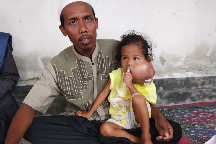 Alifa (3) bersama bapaknya, Juhaidi, sedang duduk di teras rumah, Minggu (9/6/2019)