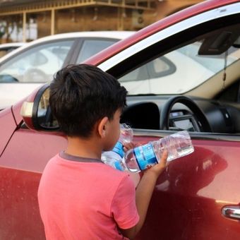 Seorang anak menjual air mineral ke pengendara mobil di jalan kota Mosu,l Irak utara, Sabtu (7/7/2018). (AFP/Waleed Al-Khalid)