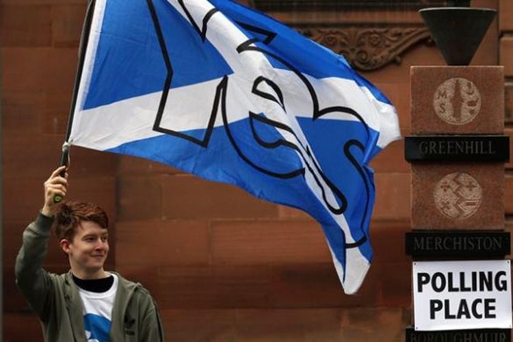 Seorang pemuda membawa bendera Skotlandia di dekat sebuah TPS sesaat sebelum referendum dimulai. Referendum yang digelar Kamis (18/9/2014) ini akan menentukan apakah Skotlandia akan menjadi sebuah negara independen atau tetap di bawah bendera Inggris Raya.