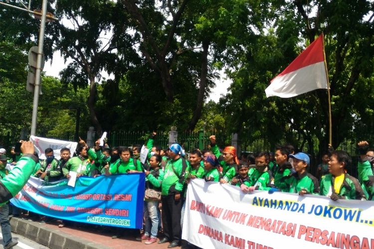 Massa ojek online membentangkan spanduk di Lapangan IRTI sebelum long march ke Kemenhub dan Istana Negara, Kamis (23/11/2017).