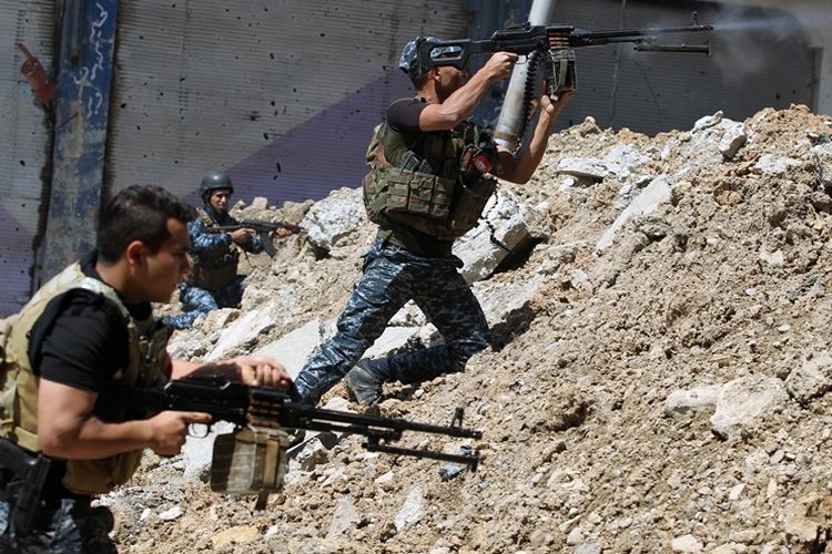 Seorang prajurit Irak melepaskan tembakan ke arah posisi ISIS sambil berlindung di belakang puing-puing bangunan di kota Mosul.