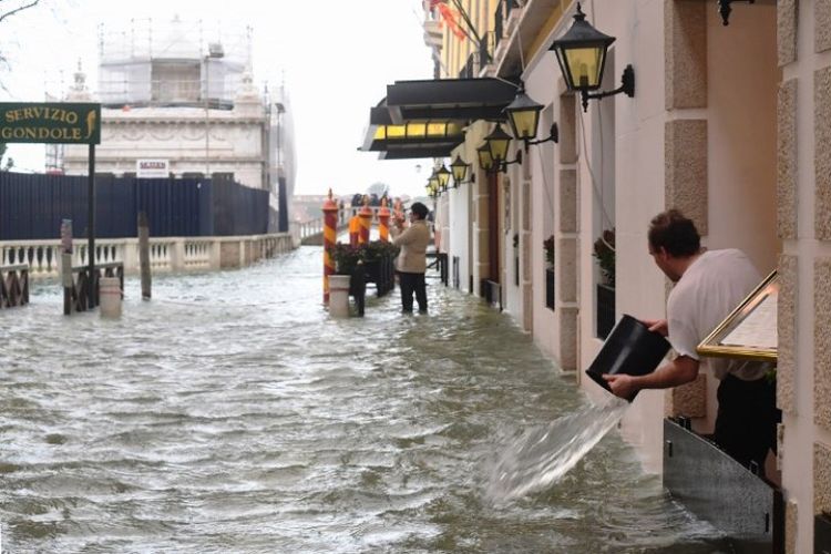 Seorang pria tampak membuang air banjir yang masuk dengan menggunakan ember di Venesia, Italia, Senin (29/10/2018). (AFP/Miguel Medina)