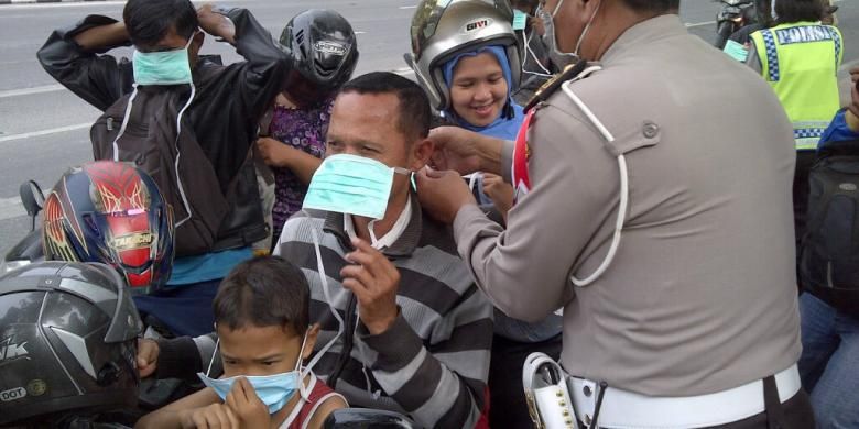 Polisi membagikan masker kepada pengendara sepeda motor di Kota Surabaya, Jumat (14/2/2014). Abu vulkanik akibat letusan Gunung Kelud juga mengguyur Kota Surabaya.